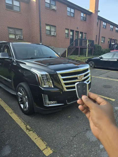A new smart key held up in front of a black Cadillac Escalade